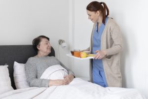 healthcare assistant bringing food on a tray to an older patient in bed 