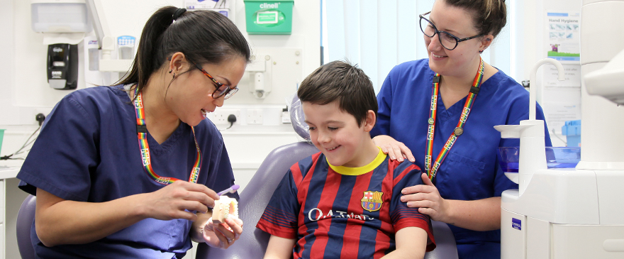 Young boy sat in a dental chair. Dentist and dental nurse alongside him.