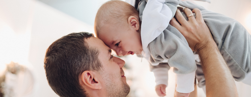 Father holding up small baby both smiling