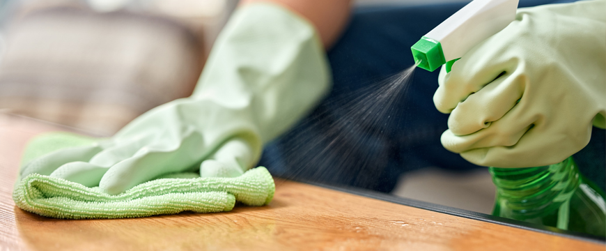 Person with cleaning gloves wiping down a surface with a disinfectant spray
