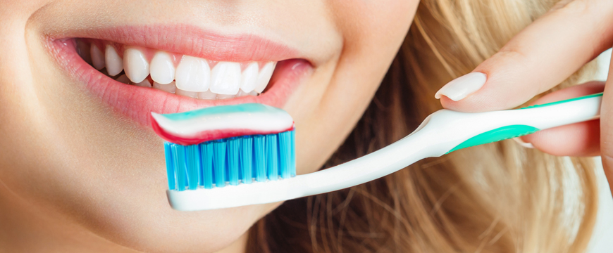 woman smiling holding a toothbrush with toothpaste on the bristles