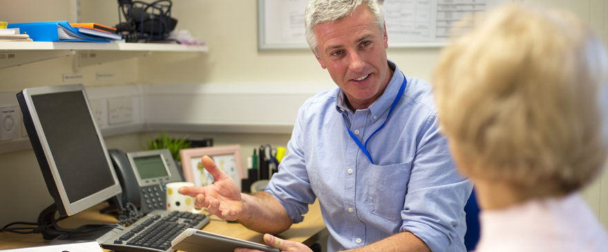 GP sat at a desk talking to a patient.