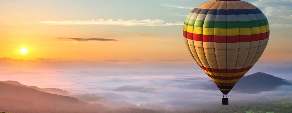 Hot air balloon flying over clouds, sunrise and mountains