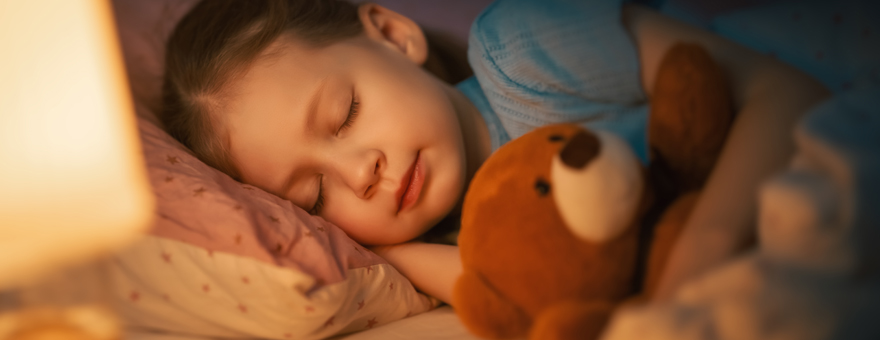 Young child asleep in bed with a teddy bear. 