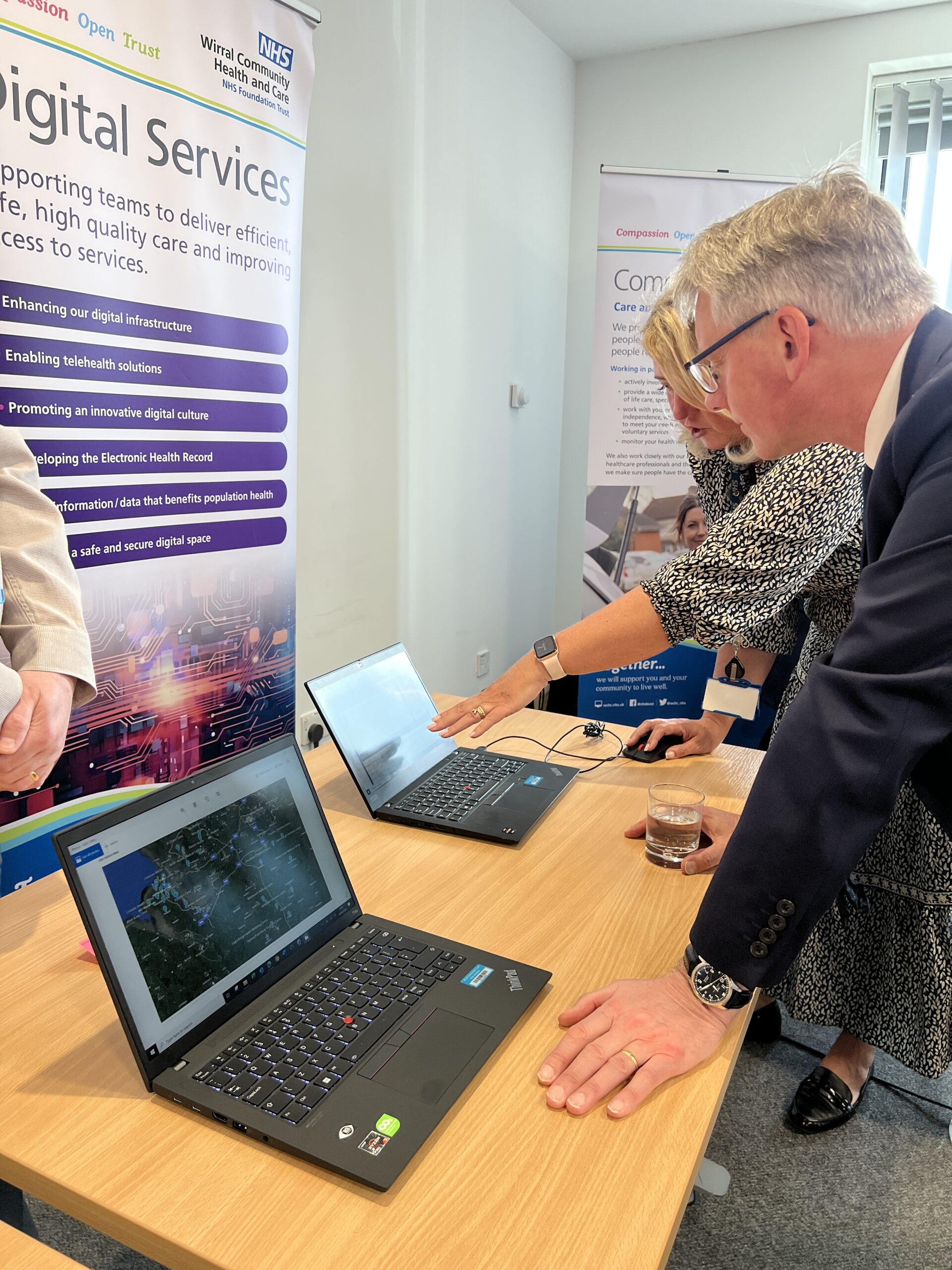 WCHC staff showcasing their work to visitors from NHS Providers. Two people looking at computer screen with data on it.