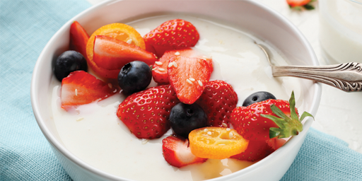 Image of a bowl of natural yoghurt topped with chopped fruit including strawberries and blueberries. 