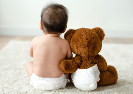 Baby in nappy next to teddy bear in nappy