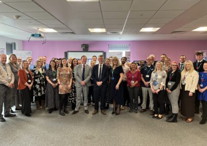 Group of NHS staff stood as a group in a large meeting room