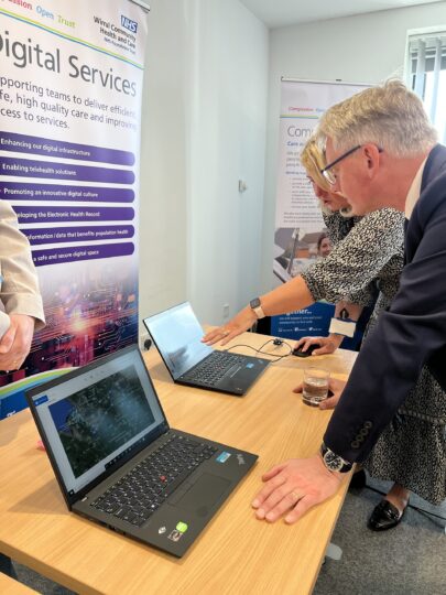 WCHC staff showcasing their work to visitors from NHS Providers. Two people looking at computer screen with data on it.