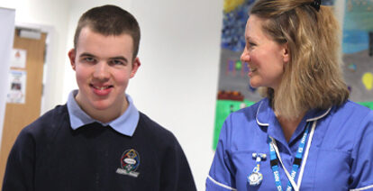 Young person in school uniform with school nurse. They are walking down a school corridor.