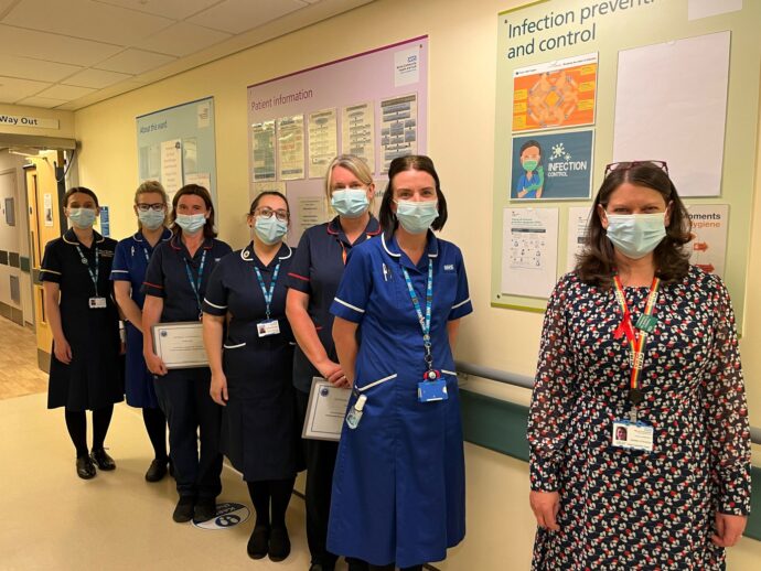 Group of clinical staff in uniform wearing face masks stood in corridor
