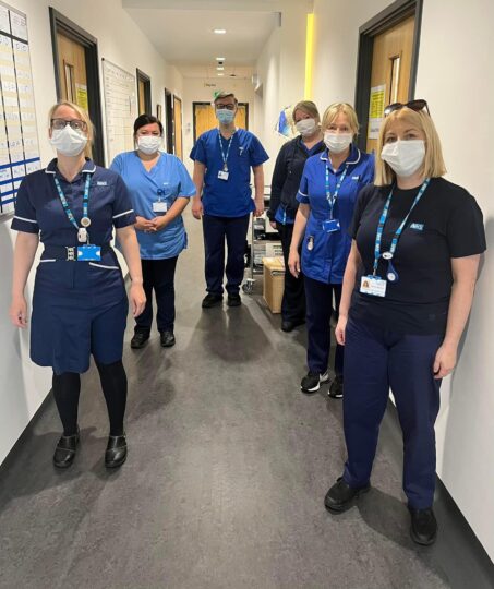 Group of clinical staff in uniform wearing face masks stood in corridor