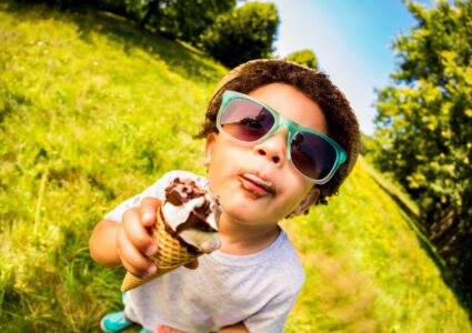 Young child eating ice cream wearing sunglasses in the sunshine