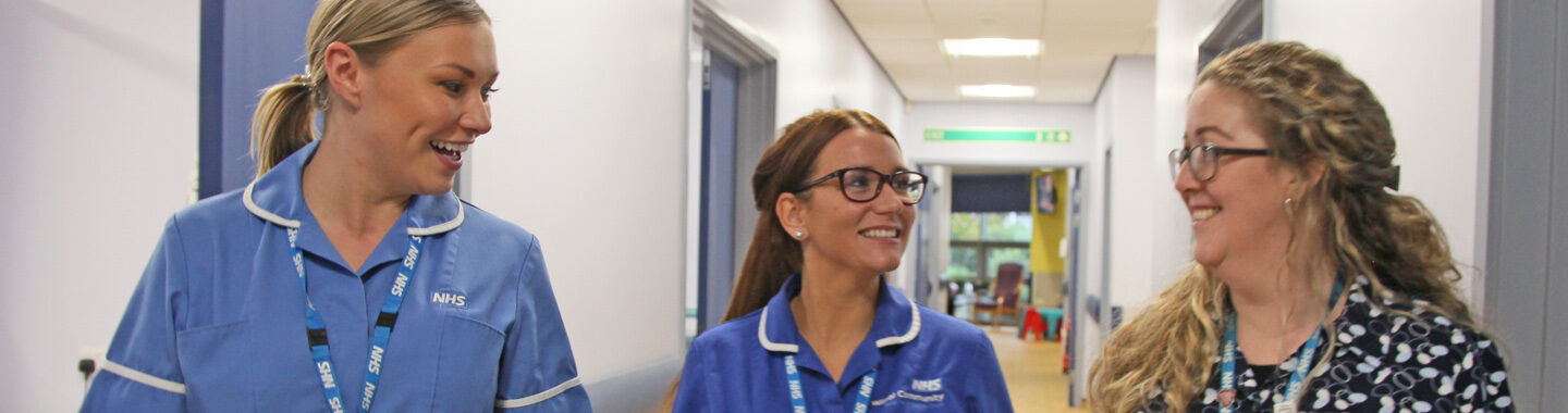 Two clinical colleagues in uniform walking down corridor with clerical colleague, smiling and chatting